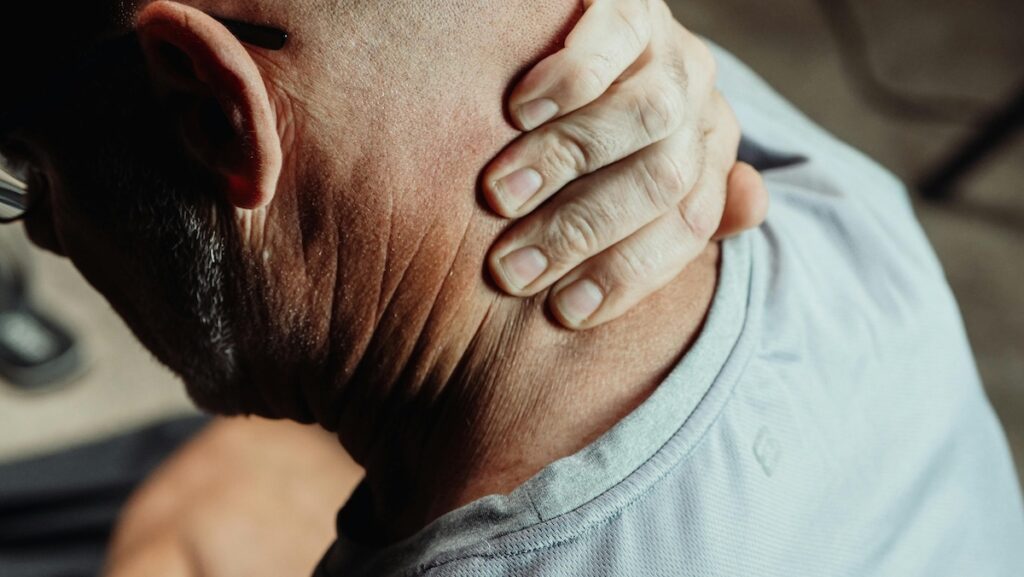 Close-up of a man holding his neck with his hand, suggesting neck pain or strain.