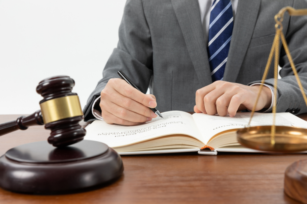 Lawyer in a gray suit signs a document at a desk with a gavel and scales of justice nearby